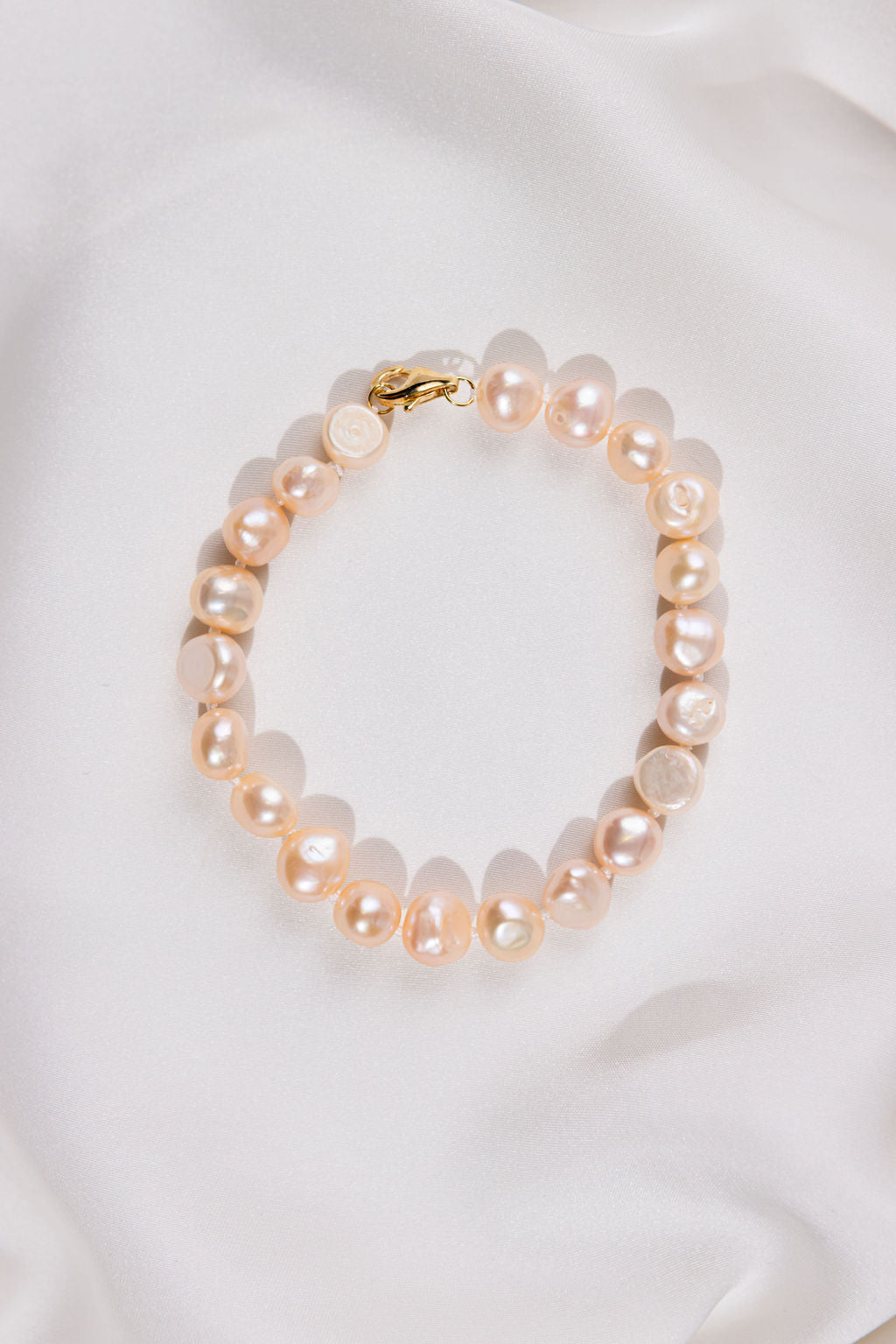 Pink Pearl bracelet with gold clasp on a white satin background